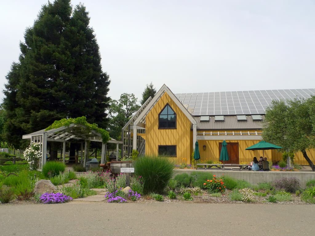 Yellow barn-style tasting room with a vine-covered pergola, umbrellas and a garden at Quivira Winery