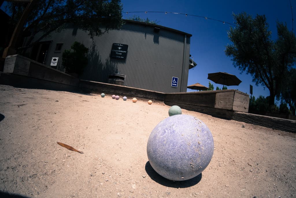Bocce court at Cornerstone Sonoma with a corrugated-metal tasting building and patio umbrellas behind (fisheye view)