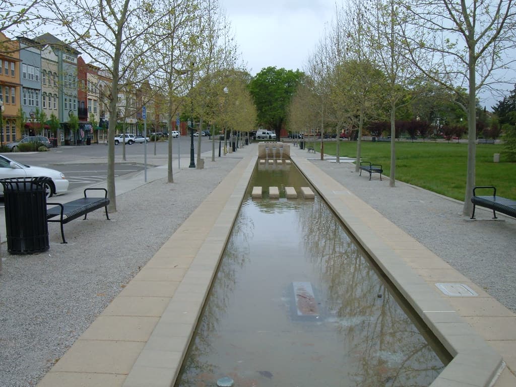 Long reflecting pool lined with benches, young trees and lawn on the Windsor Town Green