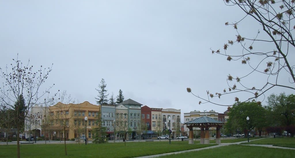 Open lawn of the Windsor Town Green with a pavilion and the colorful storefronts of McClelland Street
