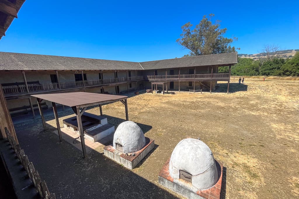 Courtyard of the Petaluma Adobe with two clay beehive ovens under a shade ramada, ringed by the adobe's two-story verandas