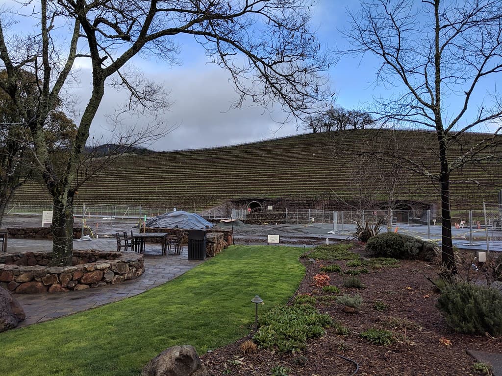 Lawn, stone-walled beds and umbrella-shaded patio tables below a terraced vineyard hill at Kunde Family Winery