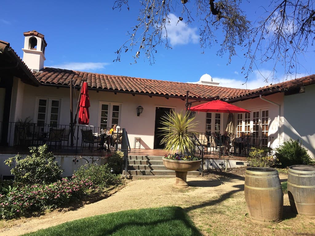 Tile-roofed estate building with red umbrellas over the terrace, barrels and lawn at Michel-Schlumberger