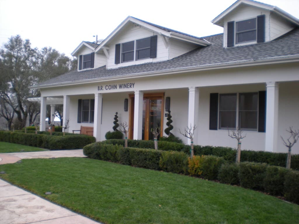 White farmhouse-style B.R. Cohn Winery tasting room with a lawn and clipped hedges