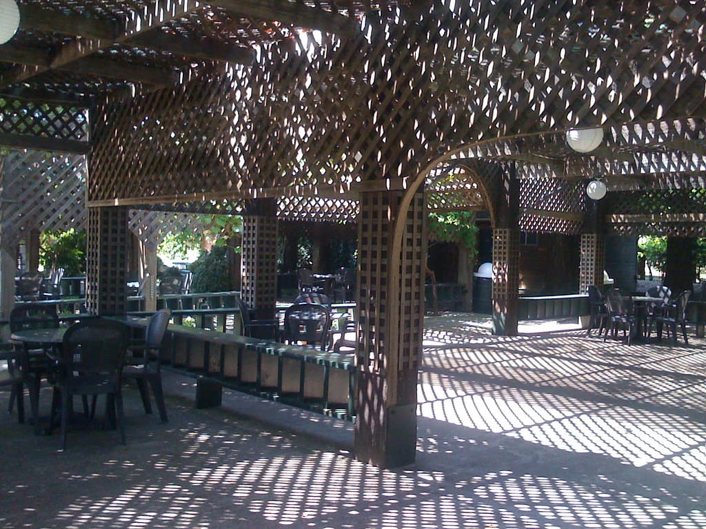Photo: Maggie M. (CC BY 2.0) Tables and chairs in dappled shade under a wooden lattice pergola beside the tasting room at Trentadue Winery