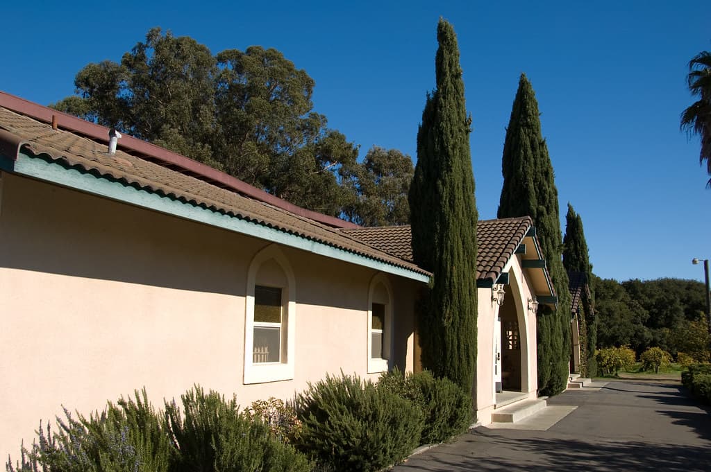 Photo: photoverulam (CC BY-SA 2.0) Stucco Madonna Estate winery building with a tiled roof and tall Italian cypresses along the drive