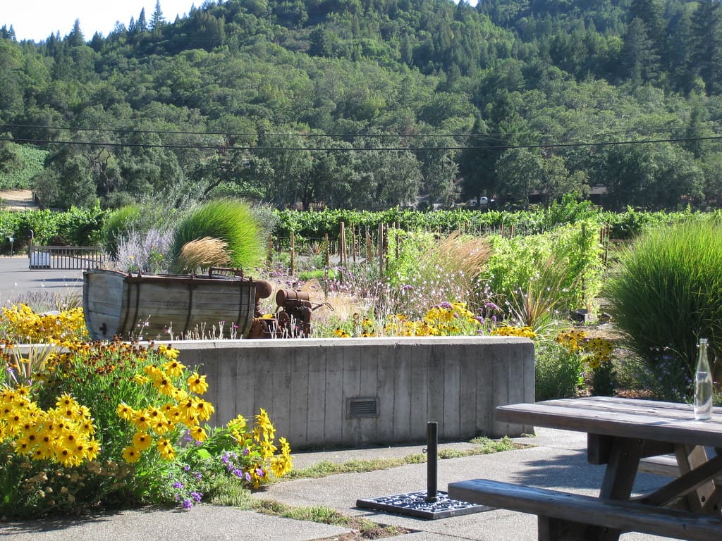 Photo: Deb Harkness (CC BY 2.0) Wooden picnic table beside flowering garden beds, with vineyards and wooded hills behind, at Quivira Vineyards