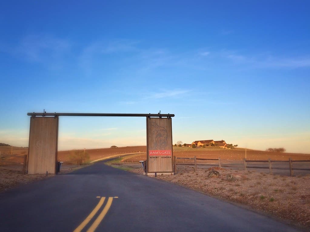 Ram's Gate entrance gate on a winding drive through golden Carneros hills at sunset, with the estate on the rise beyond