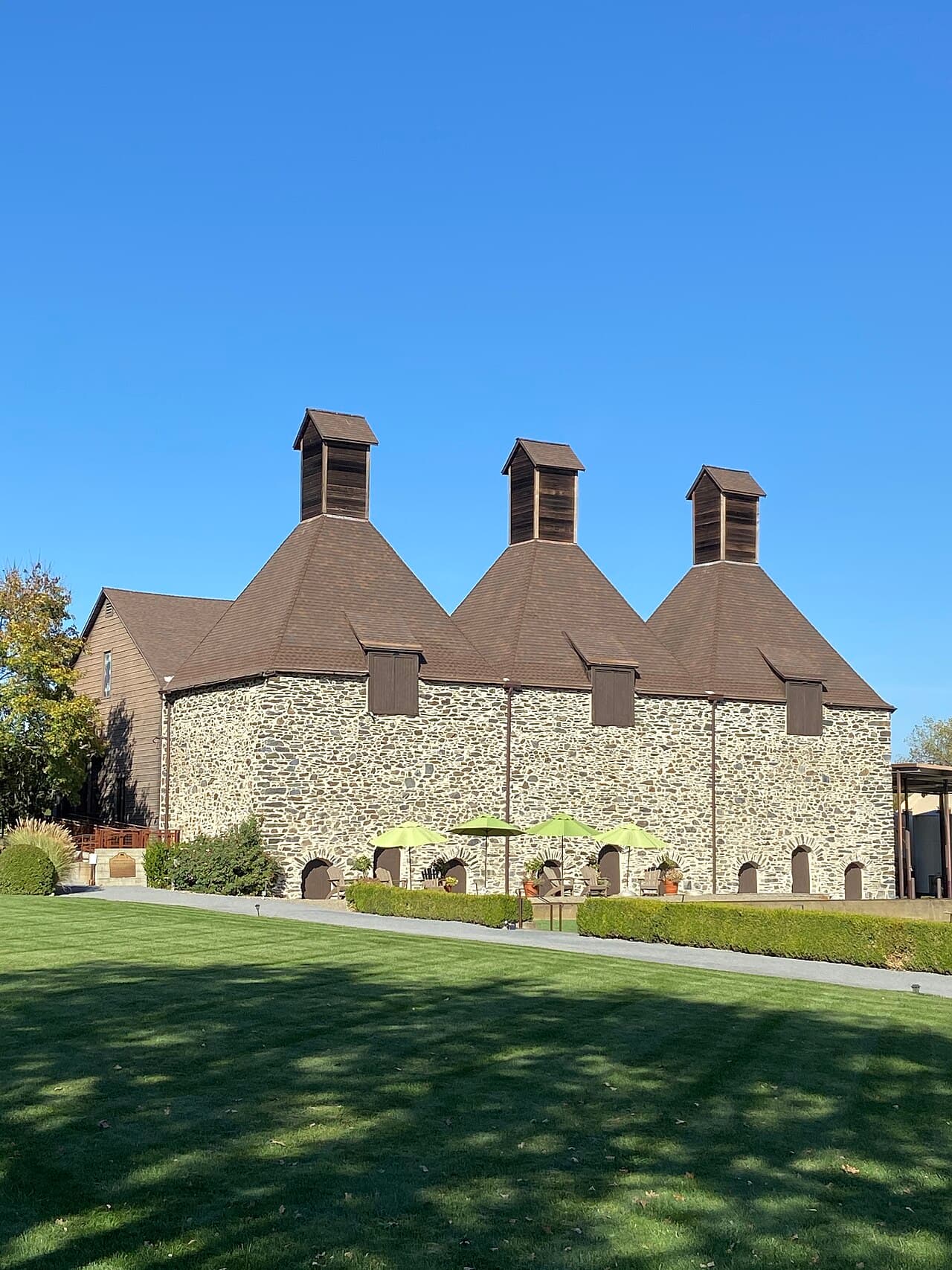 Wide lawn with umbrella-shaded tables in front of the three-towered stone hop kiln on Westside Road