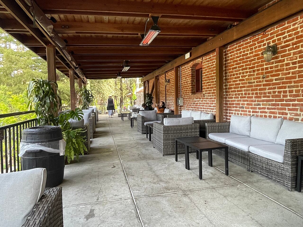 Covered brick veranda with lounge seating and barrel tables at the Korbel deli, looking out to redwoods