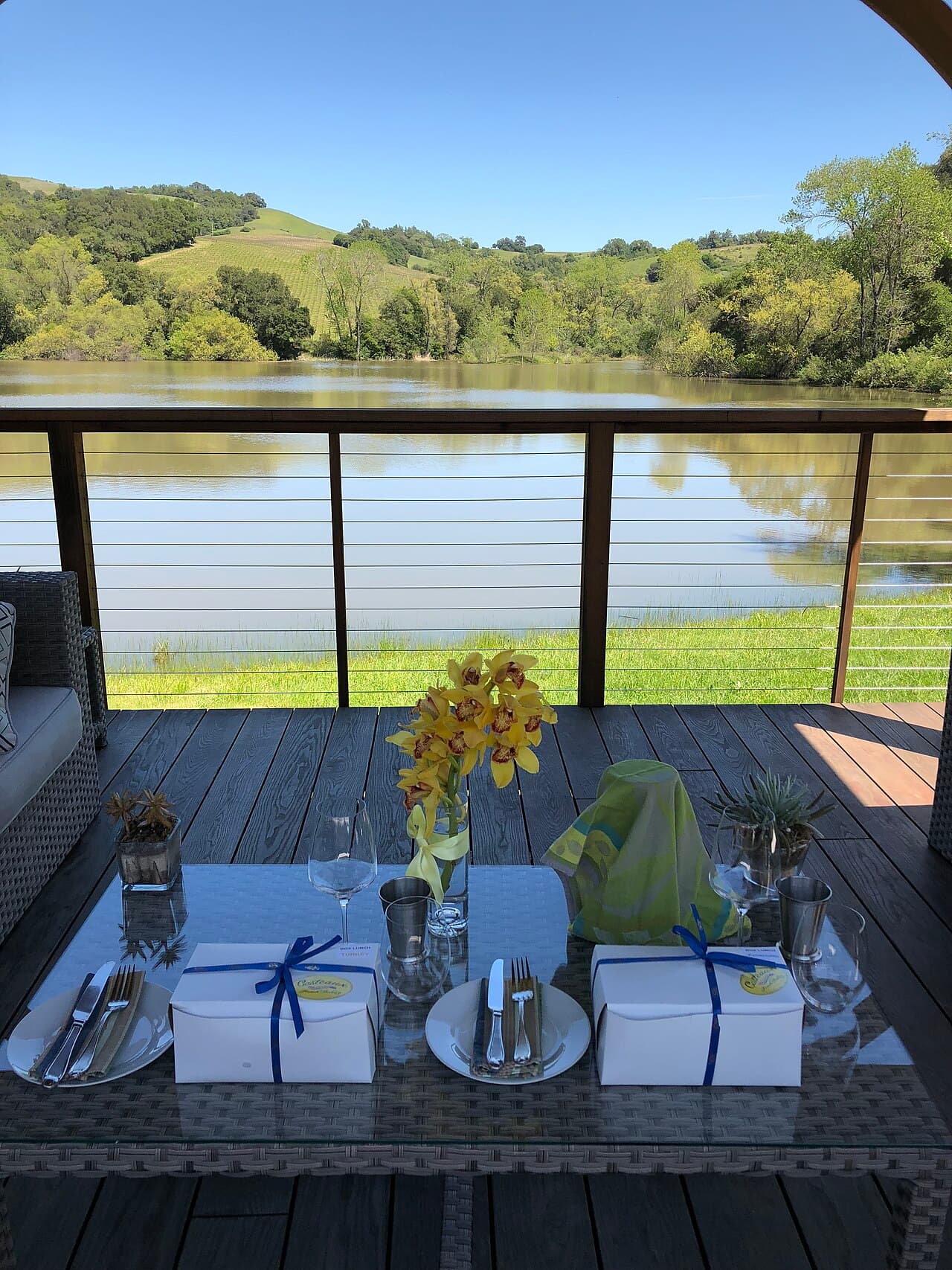 Table set with boxed lunches and flowers on a deck overlooking the lake at Notre Vue