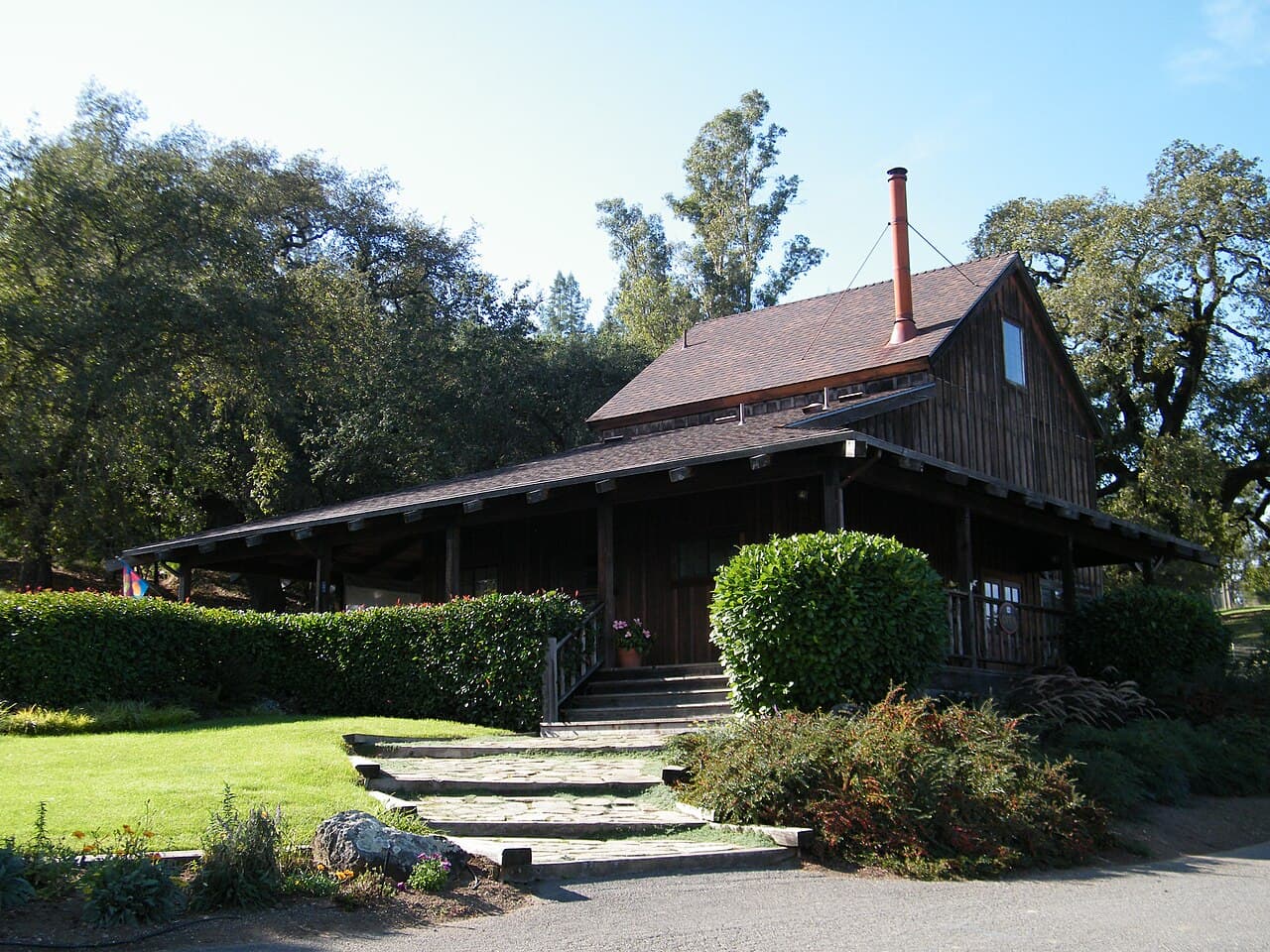 Weathered wooden Mill Creek tasting room with a covered porch among oaks and hedges