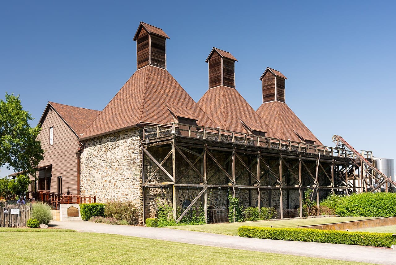 Historic stone hop kiln with three wooden towers above a clipped lawn and hedges