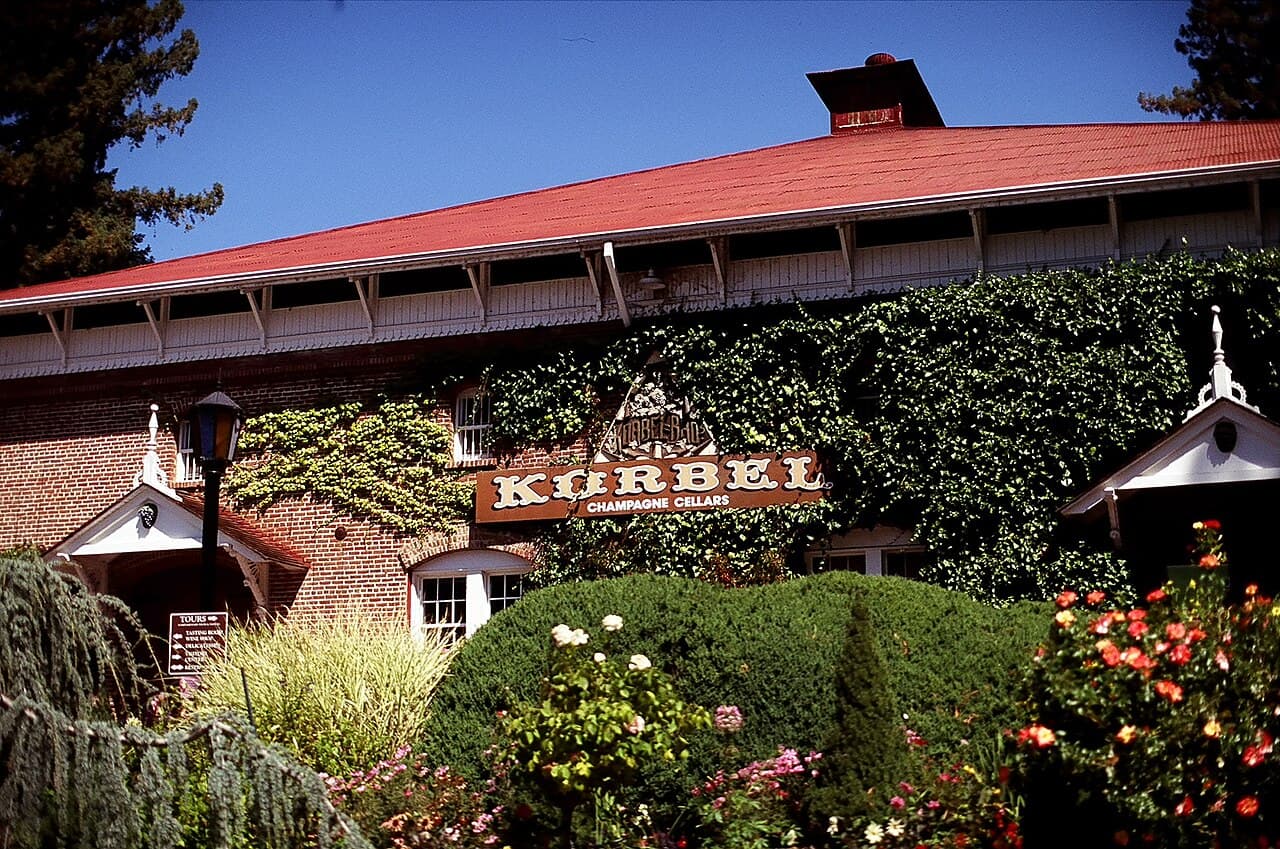 Ivy-covered brick champagne cellar with a red roof, Korbel sign and rose garden in front