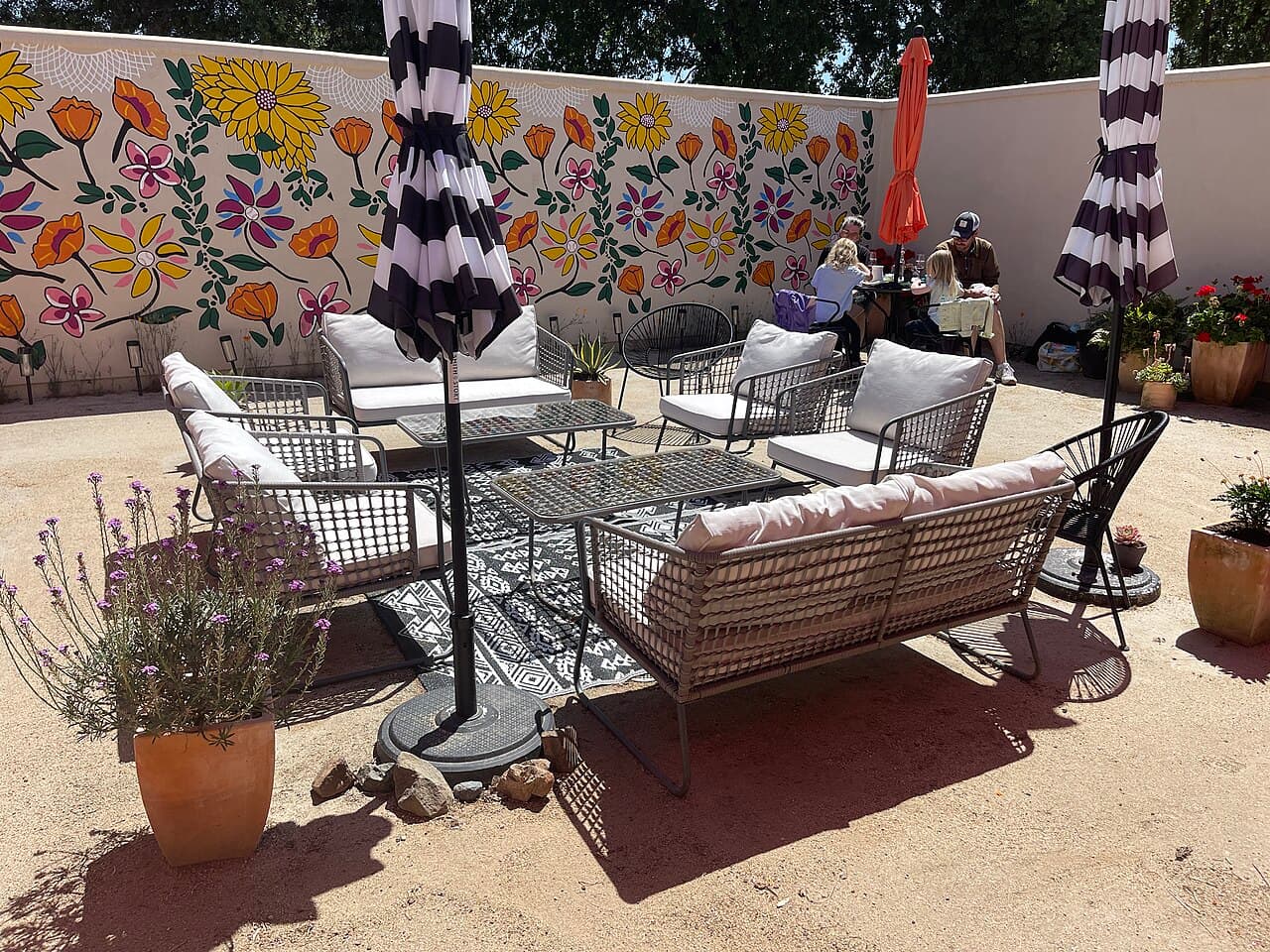 Outdoor lounge seating under striped umbrellas beside a flower mural in the Smith Story wine garden at Bacchus Landing