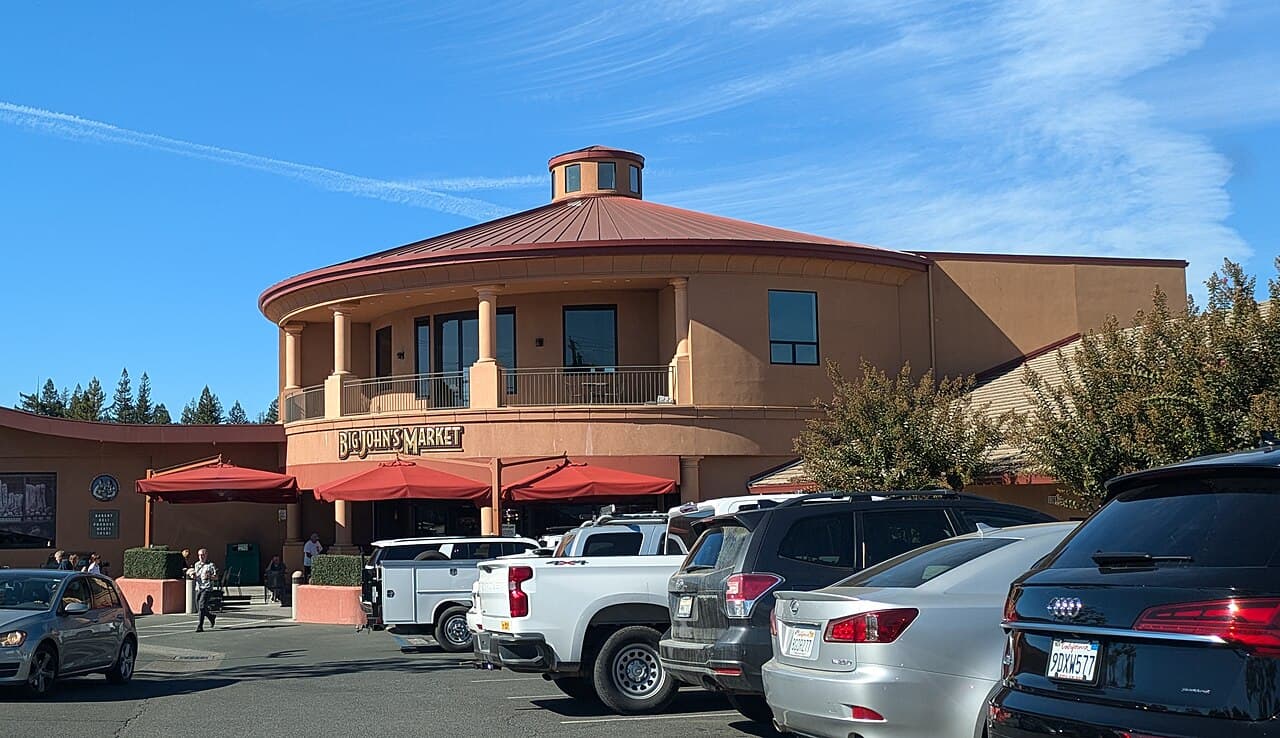 Big John's Market with its domed corner tower and red umbrellas over the outdoor tables, seen from the parking lot