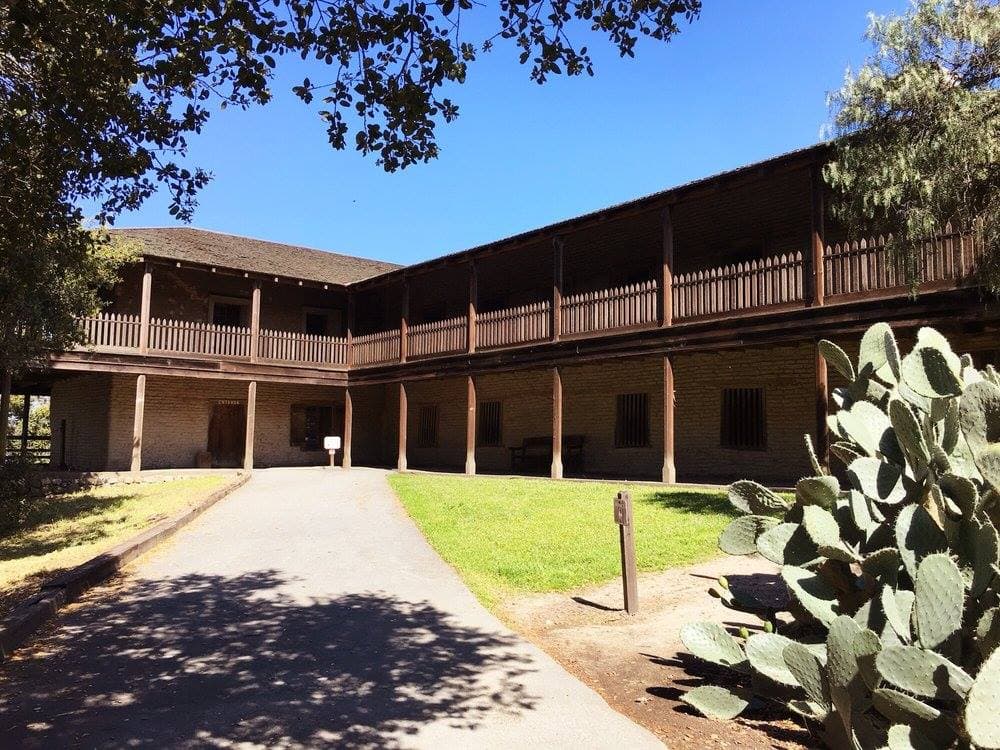 Photo: Missvain (CC BY 4.0) Two-story adobe with wooden verandas, lawn and prickly pear cactus at Petaluma Adobe State Historic Park