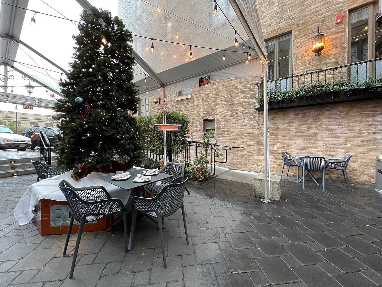 Tented courtyard with café tables and a decorated holiday tree beside the brick Hotel Petaluma, home of Costeaux Petaluma