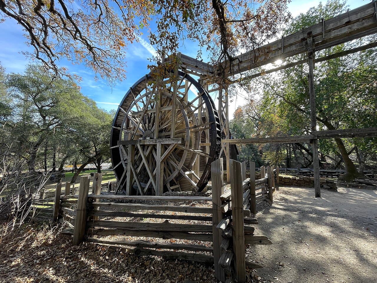 The giant wooden waterwheel and flume of the historic Bale Grist Mill behind a split-rail fence under oaks