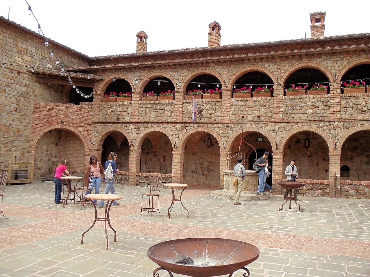 Arcaded stone courtyard with bistro tables, flower boxes and an old well at the Castello di Amorosa castle winery