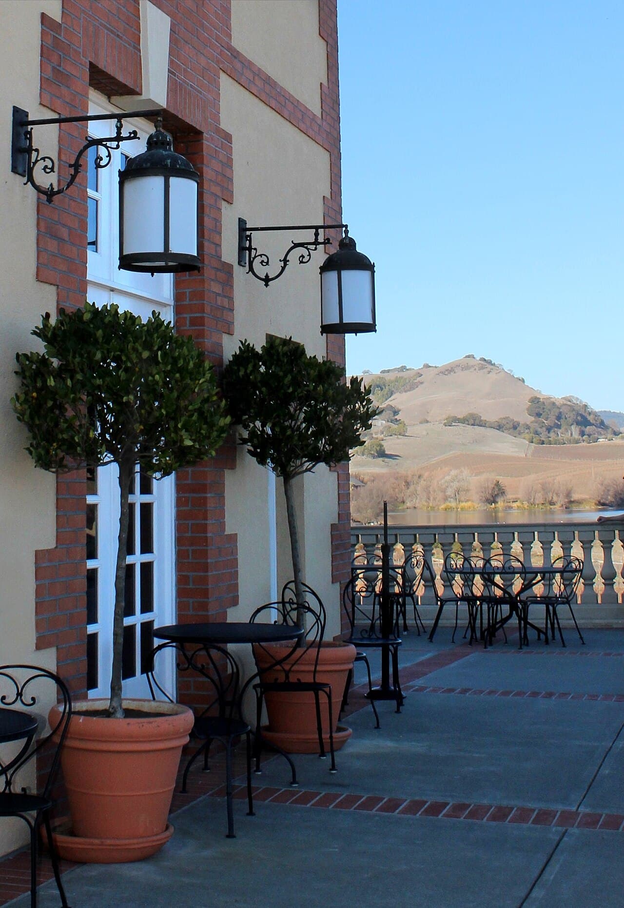 Terrace tables beside potted topiary and lanterns at Domaine Carneros, with Carneros hills beyond