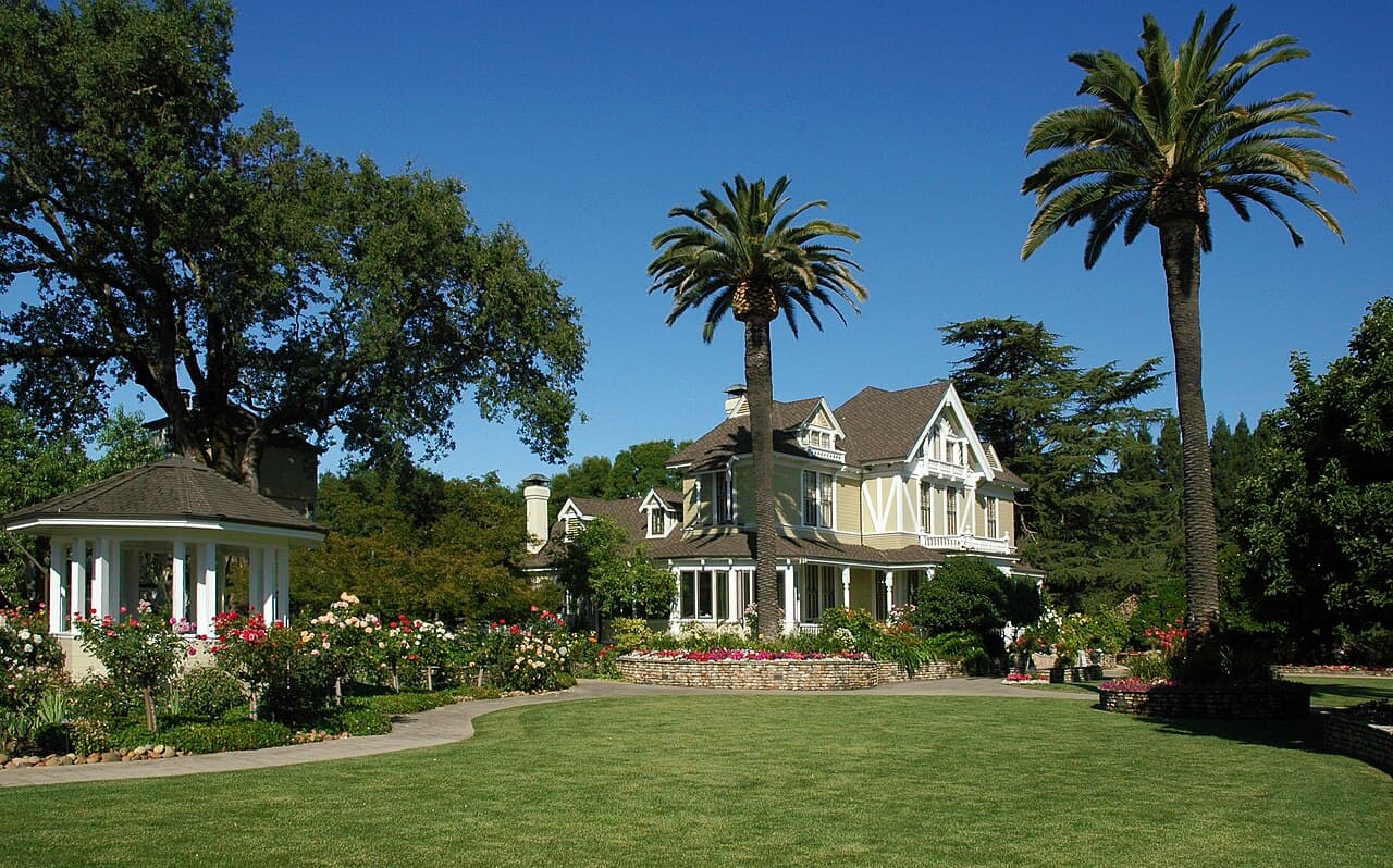 Broad green lawn, rose beds and a white gazebo in front of the Victorian house at Sutter Home Winery, framed by palms