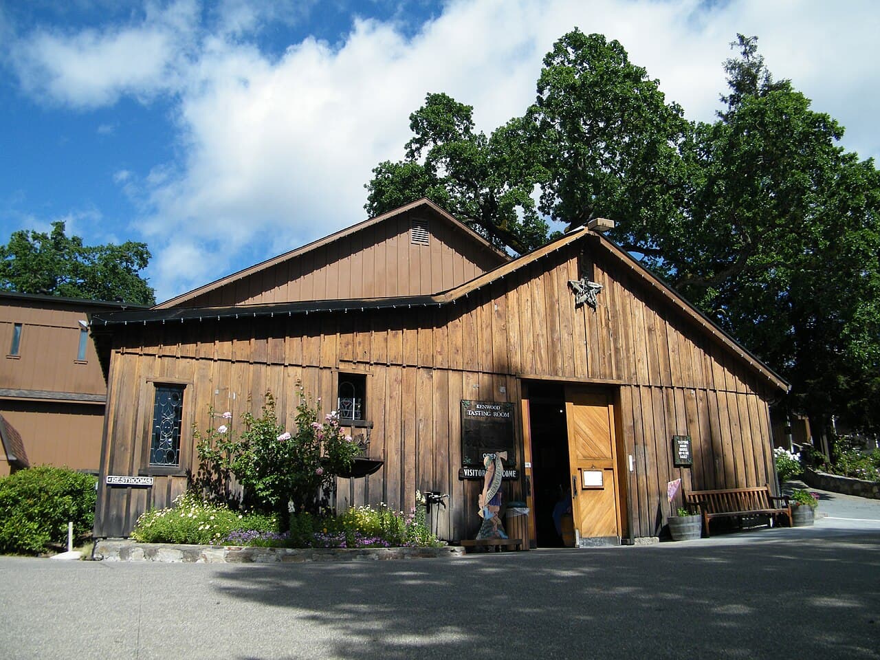 Rustic board-and-batten barn housing the Kenwood Vineyards tasting room, with climbing roses and big trees
