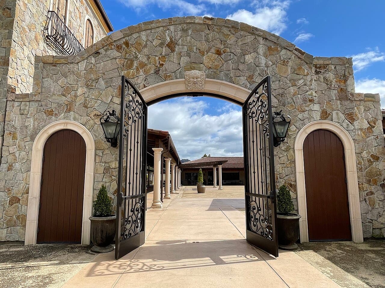 Open iron gates in a stone archway leading into the colonnaded courtyard at Bacchus Landing