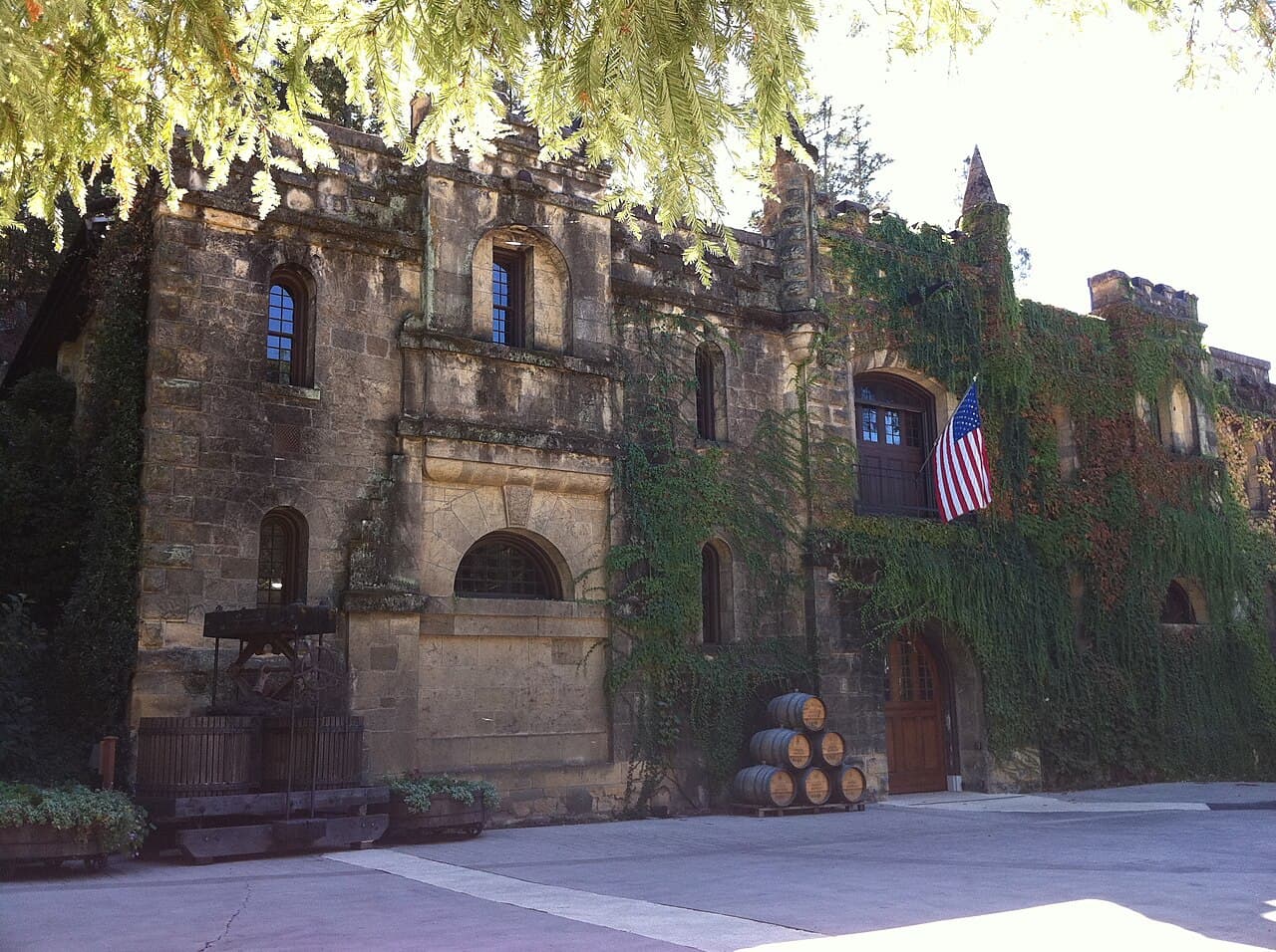 Ivy-covered stone facade of the Chateau Montelena winery with an American flag, an old basket press and stacked barrels