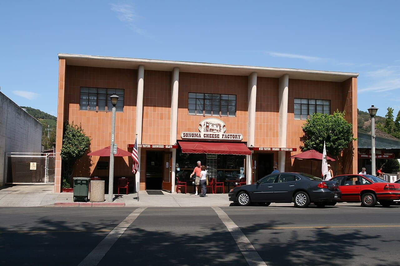 Brick-and-glass Sonoma Cheese Factory storefront with red awnings facing Sonoma Plaza