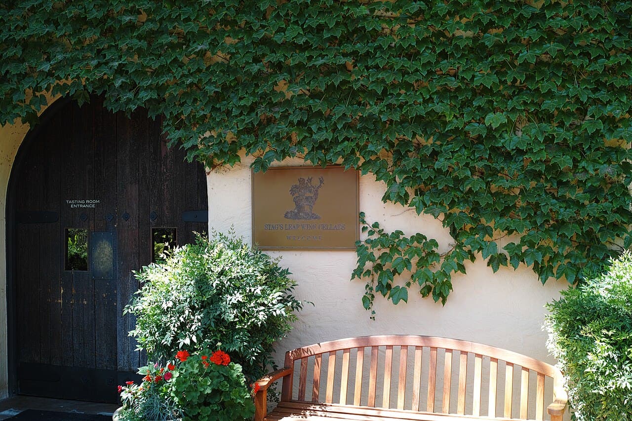 Ivy-covered tasting room entrance with a Stag's Leap Wine Cellars welcome plaque, a wooden door and a bench