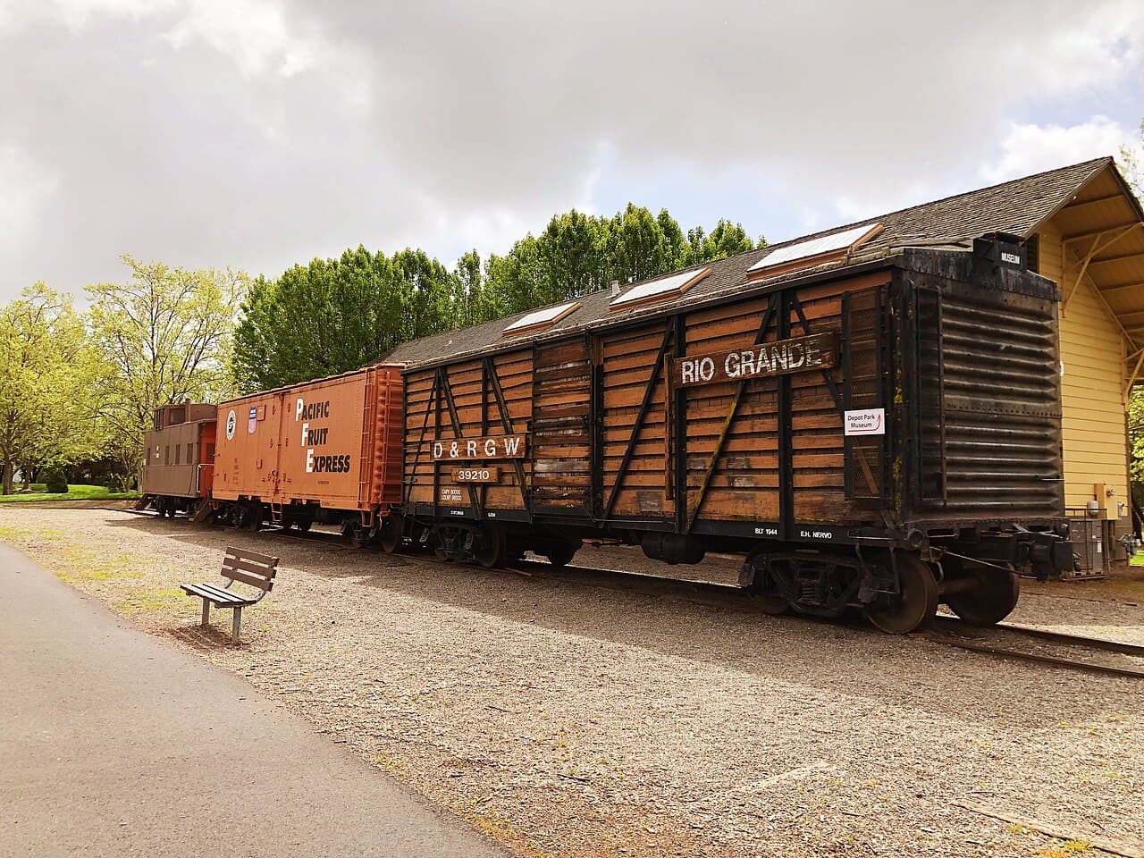 Vintage freight cars lined up beside a paved path and bench at Depot Park, Sonoma