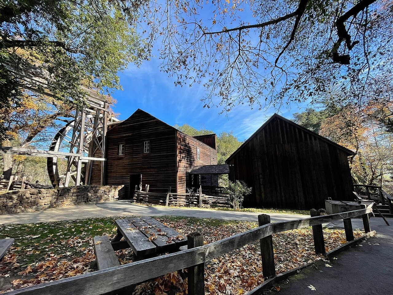 A weathered picnic table in fallen oak leaves beside the path to the wooden grist mill, granary and waterwheel at Bale Grist Mill