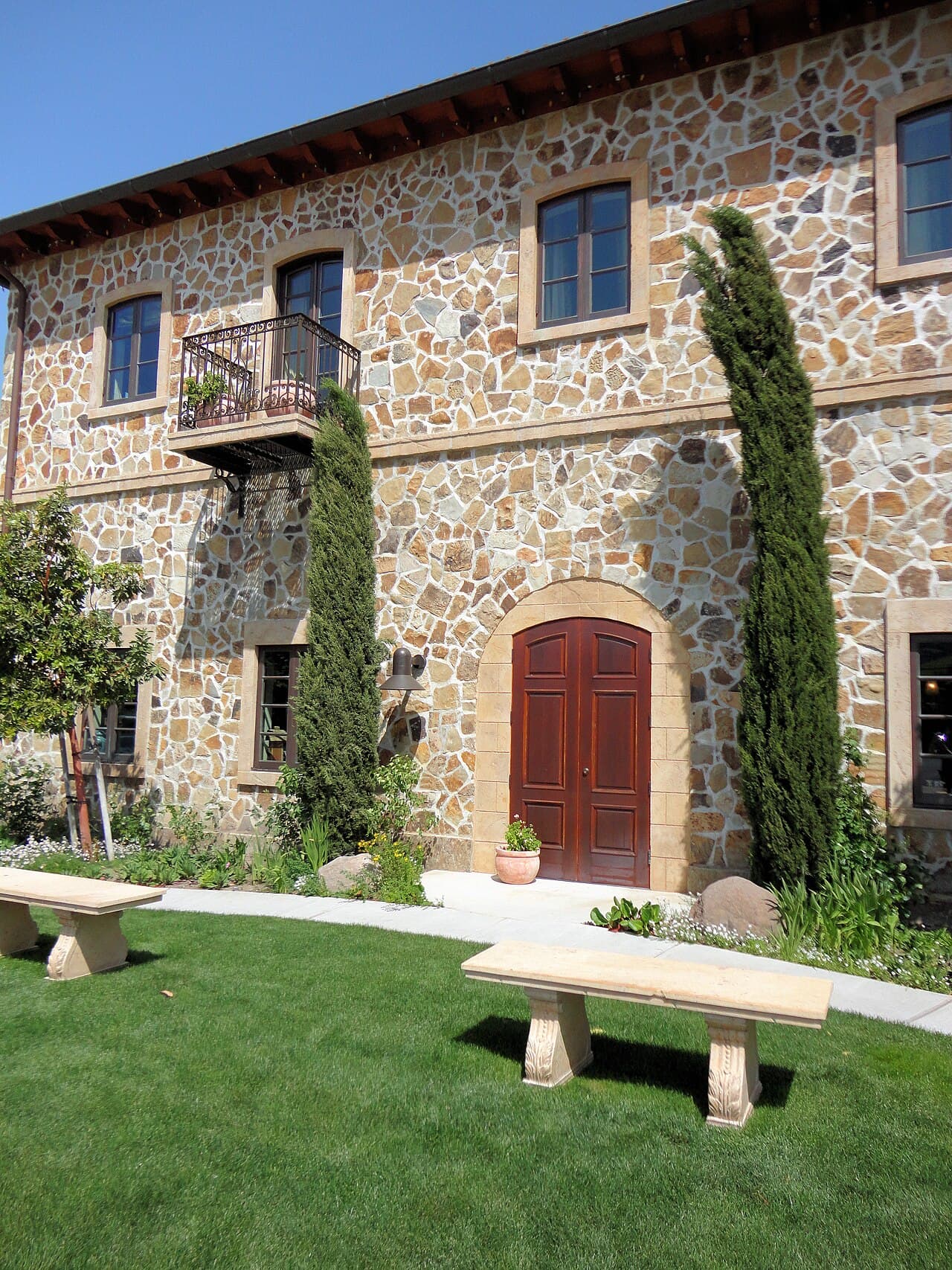 Lawn with stone benches beside the stone winery wall and cypresses at Jacuzzi Family Vineyards
