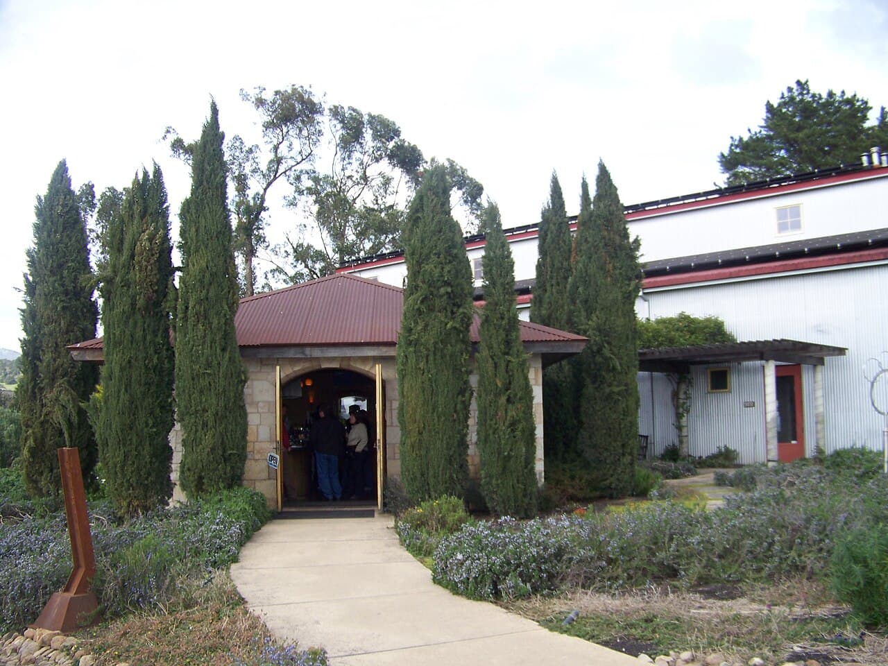 Stone tasting room entrance framed by Italian cypresses and rosemary at Hagafen Cellars