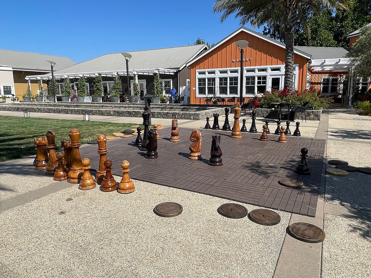 Giant chess set on a patio beside the lawn and farmhouse-style buildings at Carneros Resort's Town Square