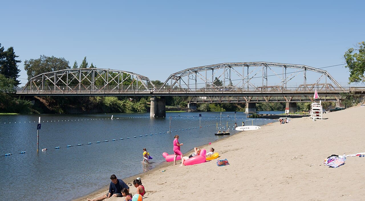 Swimmers and sunbathers on the sandy Russian River beach below the steel Healdsburg Memorial Bridge