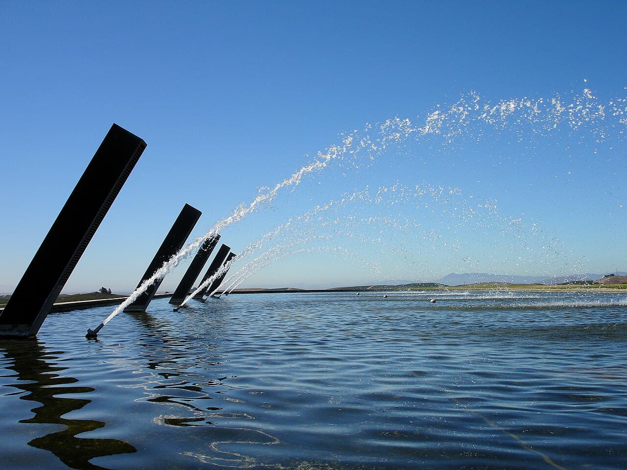 Arcing fountain jets over a reflecting pool against a blue sky at Artesa Winery