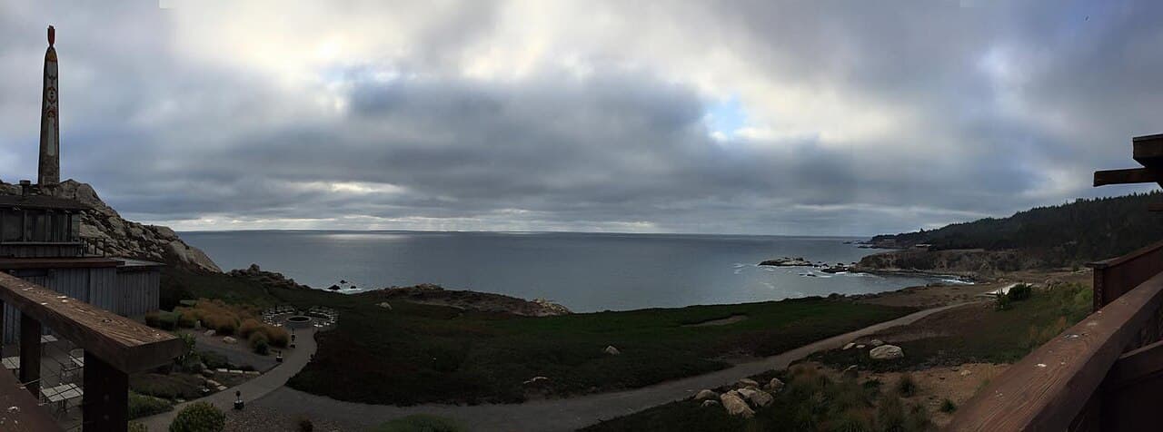 Panoramic view from Timber Cove Inn over the landscaped bluff, cove and Pacific under a cloudy sky