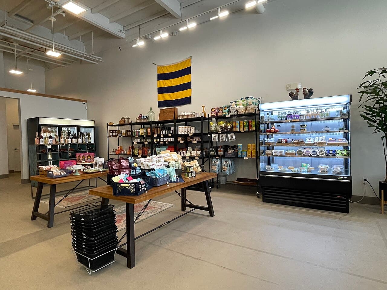 Inside Deuces Market in Napa: wooden display tables of snacks, shelves of pantry goods and a lit grab-and-go fridge case