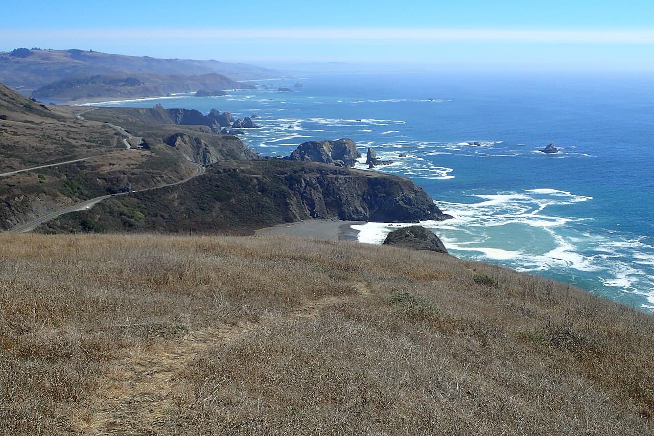 Dry grassy bluff above a rugged coastline of sea stacks, coves and surf seen from the Vista Trail on the Sonoma Coast
