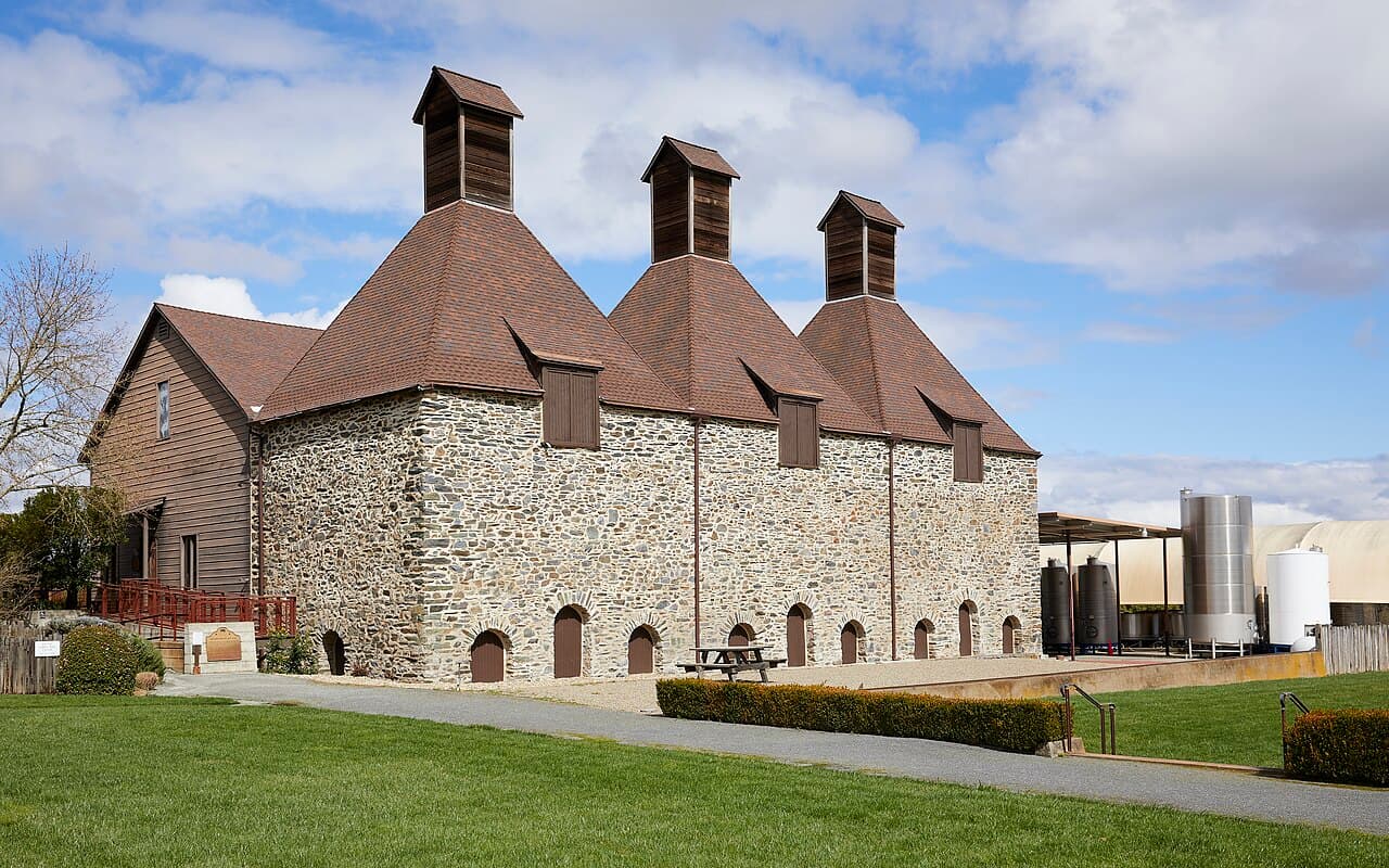 Historic stone hop kiln with three wooden towers, picnic table and lawn at Landmark's Hop Kiln Estate