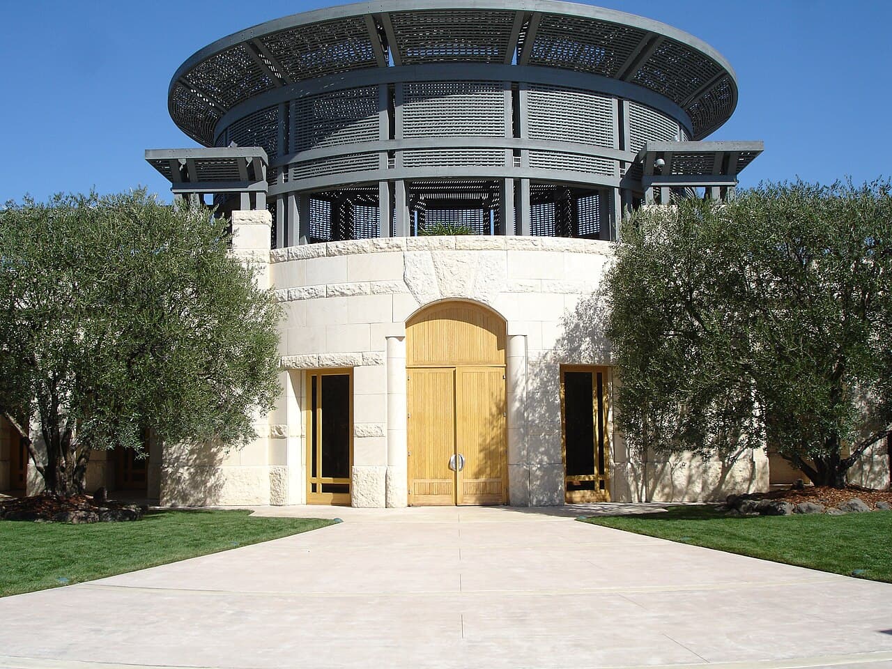 Pale limestone entrance with tall wooden doors and olive trees beneath the circular colonnade at Opus One