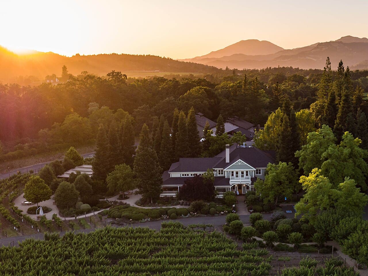 Aerial view at sunset of the Duckhorn Vineyards Estate House among gardens, trees and vineyard rows, with the Mayacamas hills behind